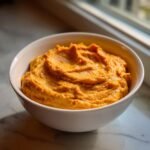 A close-up of thick, vibrant orange Pumpkin Peanut Butter Dip served in a white bowl.