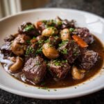 Close-up of tender chunks of Beef Bourguignon stewed in dark sauce with mushrooms and carrots, garnished with parsley.