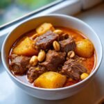 Close-up of a bowl of rich, savory Massaman Curry featuring tender beef chunks, yellow potatoes, and whole peanuts.