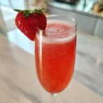 A vibrant, bubbly Rossini Cocktail served in a flute glass, garnished with a fresh strawberry.