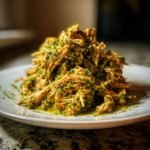 A mound of shredded chicken coated in vibrant green salsa verde sauce, served on a white plate.