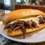A delicious sandwich filled with shredded Slow Cooker Italian Beef and melted white cheese on a hoagie roll.