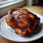 A whole, beautifully browned Spatchcock Grilled Chicken resting on a white plate indoors.