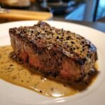Close-up of a medium-rare Steak Au Poivre covered in creamy peppercorn sauce.