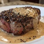 Close-up of a thick-cut steak crusted with peppercorns, covered in creamy sauce, a perfect Steak Au Poivre.