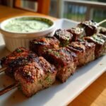 Close-up of perfectly grilled Steak Mushroom Kabobs served next to a bowl of bright green mint yogurt dip.