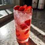 A tall glass filled with a bright pink Strawberry Acai Refresher, ice, and fresh strawberry slices.