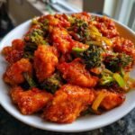 Close-up of crispy, glazed Szechuan Chicken pieces mixed with bright green broccoli florets in a white bowl.
