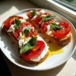 Three pieces of toasted bread topped with creamy burrata, roasted tomatoes, and fresh basil for a Tomato Burrata Salad.