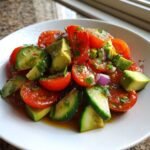 Close-up of a vibrant Tomato Cucumber Avocado Salad tossed in a light dressing, served in a white bowl.