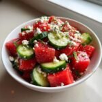 Close-up of Watermelon Cucumber Salad With Goat Cheese cubes and slices in a white bowl.
