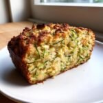 Close-up of a thick slice of moist Zucchini Bread With Apples showing shredded zucchini and a golden crust.