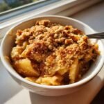 Close-up of a warm apple crumble dessert with a crunchy topping served in a white bowl, one of the Desserts That Start With A.