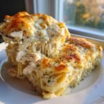 A serving of rich Chicken Alfredo Casserole being lifted, showing extreme cheese pull and golden baked topping.