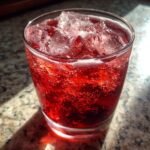 Close-up of a glass filled with bright red, fizzy Cherry Vanilla Fizz and plenty of ice cubes.