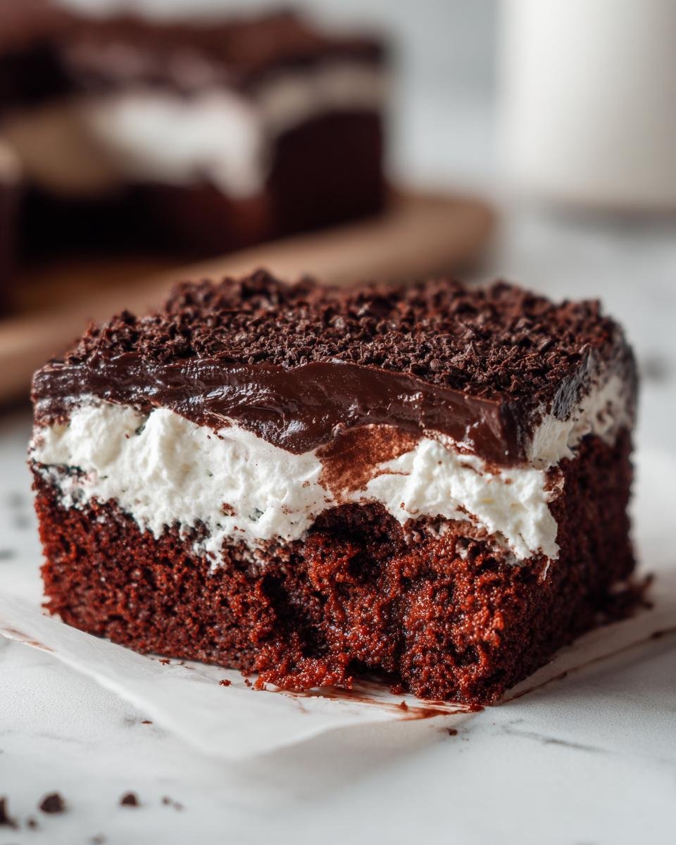 Close-up of a rich slice of Chocolate Poke Cake showing moist dark cake, white whipped cream, and chocolate ganache topping.