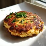 A golden-brown, perfectly seared Easy Crab Cake topped with fresh chopped parsley, sitting on a white plate.