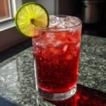 A tall glass filled with a bright red, fizzy Easy Valentines Day Mocktail, garnished with a fresh lime wheel.