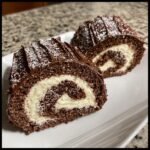 Two slices of chocolate Yule Log cake, showing the dark chocolate sponge and white cream swirl, dusted with powdered sugar.