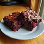 Two rich, fudgy Strawberry Brownies with visible pieces of bright red strawberries baked inside, served on a white plate.