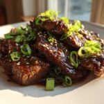 Close-up of glossy, saucy Beef Teriyaki pieces garnished with sesame seeds and sliced green onions.