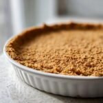 Close-up of a perfectly pressed graham cracker desserts base in a white fluted pie dish.