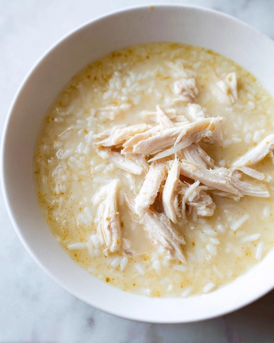 Close-up of a white bowl filled with Greek Lemon Chicken Soup, featuring rice and shredded chicken breast.