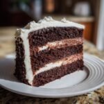 A decadent slice of three-layer Holy Cow Cake featuring dark chocolate layers and white and chocolate frosting.