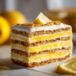 A tall, layered slice of Lemon Icebox Cake showing graham cracker layers and bright yellow lemon filling.
