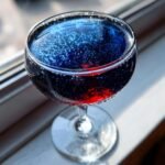 Close-up of a vibrant, bubbly Love Potion 9 Cocktail with deep blue and red layers in a coupe glass.