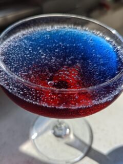 Close-up of a bubbly Love Potion 9 Cocktail showing distinct red and blue layers in a coupe glass.