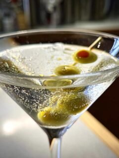 Close-up of a clear, chilled Martini in a coupe glass garnished with green olives, a perfect example of Vodka Cocktails.