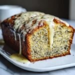 Close-up of a slice of moist Lemon Poppy Seed Bread topped with a thick, dripping lemon glaze.