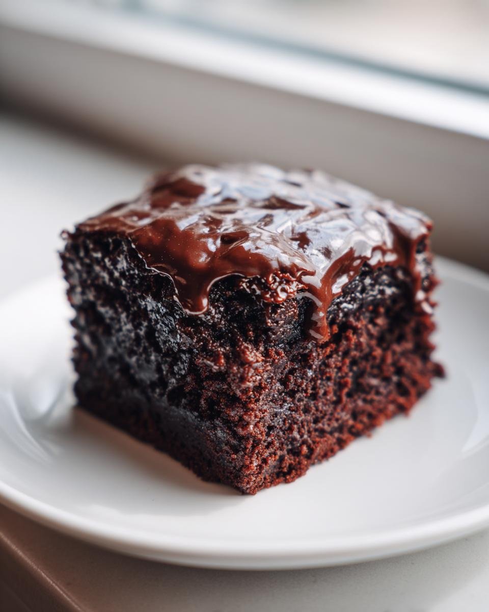 Close-up of a moist, dark chocolate slice of Texas Sheet Cake topped with glossy, dripping chocolate frosting.
