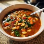 Close-up of a steaming bowl of Olive Garden Minestrone Soup filled with vegetables, beans, and pasta.