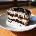 A decadent slice of Oreo Icebox Cake featuring layers of cream and chocolate cookies on a white plate.