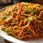 Close-up of a plate piled high with glossy Panda Express Chow Mein noodles, carrots, and green onions.