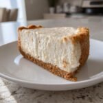 A thick slice of creamy Philadelphia No Bake Cheesecake with a graham cracker crust on a white plate.