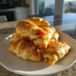 A stack of golden, flaky crescent rolls filled with pizza ingredients, served as Pizza Appetizers.
