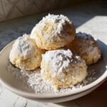 A stack of round, buttery Spanish Christmas Desserts cookies heavily dusted with powdered sugar on a light plate.