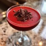 Close-up of a vibrant, deep red Red Velvet Martini garnished with a mound of dark chocolate shavings in a coupe glass.
