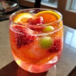 Close-up of a fizzy Rose Sangria Mocktail filled with strawberries, orange slices, and green grapes.