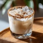 A creamy, iced RumChata drink garnished with a thick cinnamon sugar rim, served on a wooden tray.