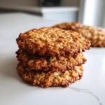 A close-up stack of three golden brown, soft Banana Oatmeal Cookies on a white countertop.