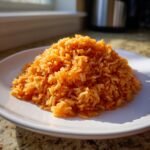 A mound of vibrant orange Spanish Rice served on a white plate, catching bright sunlight.