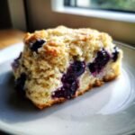 A close-up, appetizing shot of a single Starbucks Blueberry Scones piece on a light plate, showing visible blueberries.