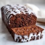 A close-up of a moist Starbucks Gingerbread Loaf, sliced, showing the rich brown crumb and white vanilla icing drizzle.