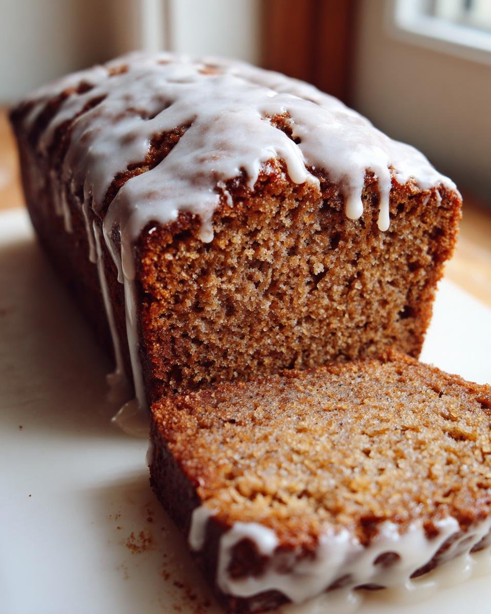 Close-up of a sliced Starbucks Gingerbread Loaf drizzled generously with white vanilla icing.
