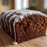 Close-up of a rich, dark Starbucks Gingerbread Loaf drizzled with white icing on a wooden board.