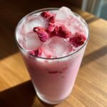 A tall glass filled with a pink, creamy Starbucks Pink Drink, ice cubes, and topped with dried red berries.